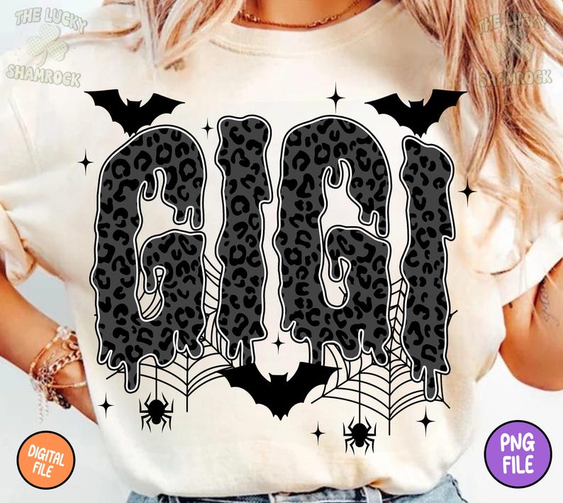 May include: Cream-colored t-shirt featuring the word "GIGI" in a dripping, leopard-print design. The shirt includes bat and spiderweb graphics, with bats and spiders. The design has a Halloween theme.