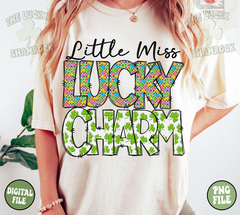 Peut inclure: Un t-shirt blanc avec le texte "Little Miss Lucky Charm" en lettres noires soulign&eacute;es. Le mot "Lucky" est d&eacute;cor&eacute; d'un motif de tr&egrave;fles &agrave; quatre feuilles color&eacute;s. Le mot "Charm" est d&eacute;cor&eacute; de motifs de tr&egrave;fles &agrave; quatre feuilles verts.