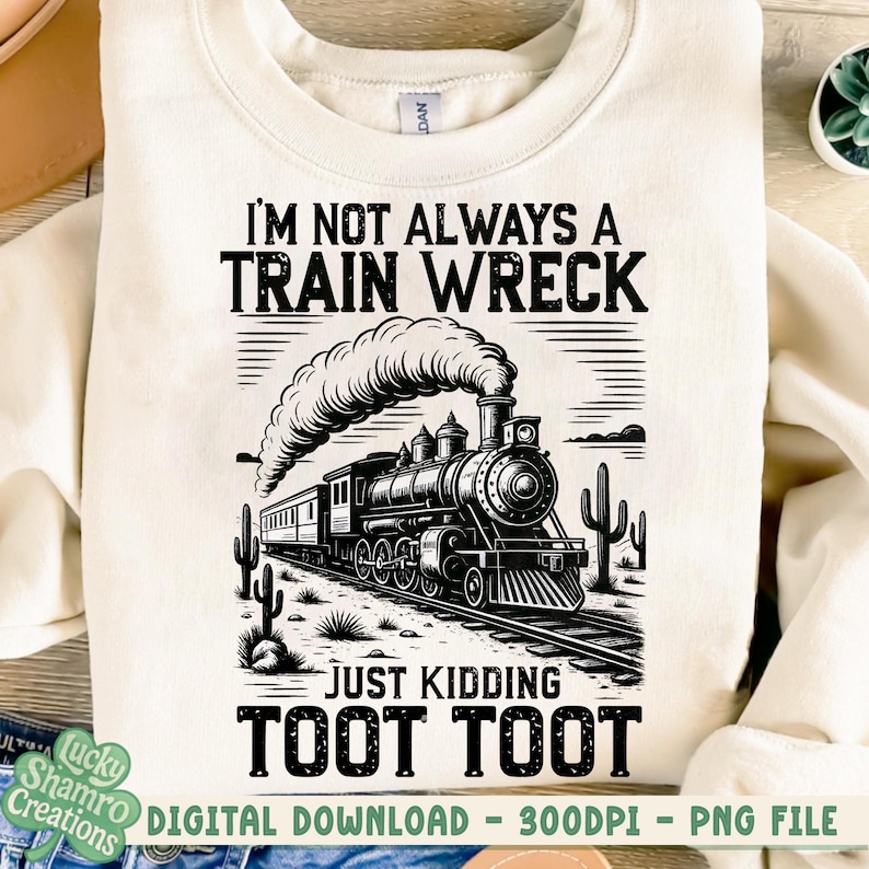 K&ouml;nnte beinhalten: Cremefarbenes Sweatshirt mit einer schwarz-wei&szlig;en Grafik einer alten Dampflok. Der Text lautet: "I'M NOT ALWAYS A TRAIN WRECK JUST KIDDING TOOT TOOT". Das Design umfasst Kakteen und Bahngleise.