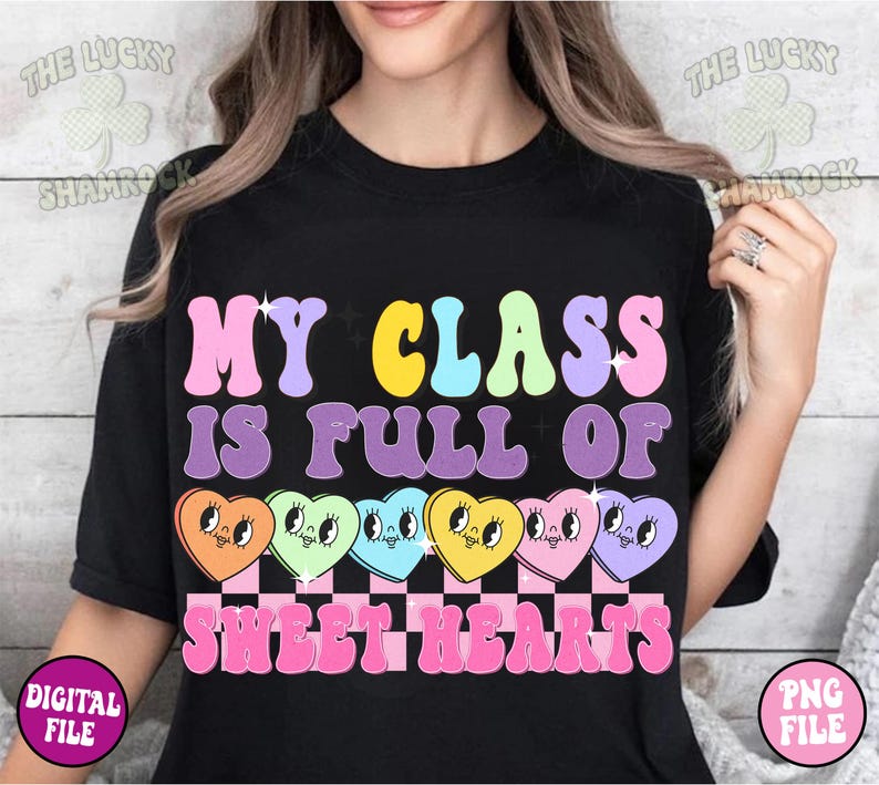 May include: Black t-shirt with the text "My Class Is Full Of Sweethearts" in rainbow colors. The text is surrounded by a row of six cartoon candy hearts with faces.
