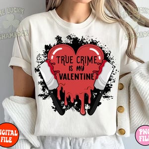May include: White t-shirt with a red heart graphic that says "True Crime is my Valentine". The heart is dripping with red and has two black knives on either side.