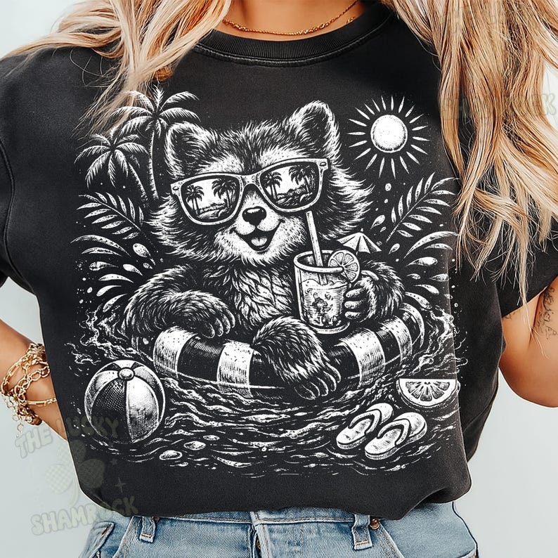 May include: Black graphic t-shirt featuring a raccoon wearing sunglasses and floating in a pool with a drink. The raccoon is in a black and white inner tube. Palm trees, a beach ball, and flip-flops are also in the design.
