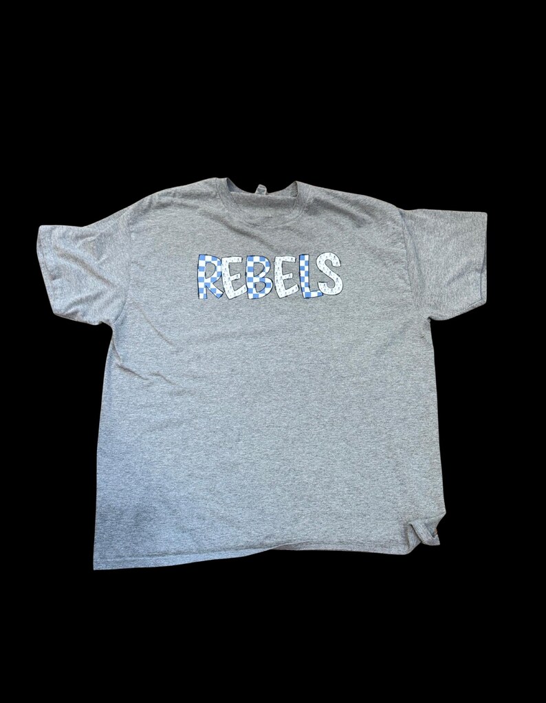 May include: A gray t-shirt with the word "REBEL" printed in blue and white checkered letters.