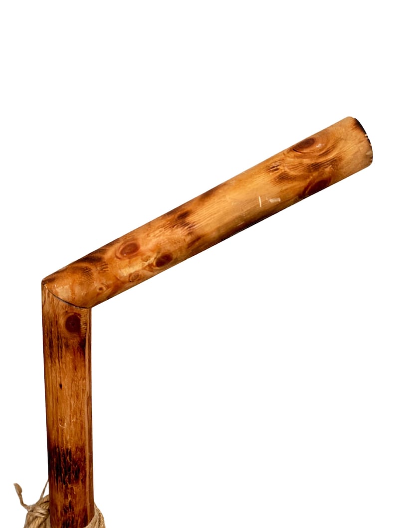 May include: A wooden stick bent at a 90-degree angle, with a natural brown finish. The stick is tied with a brown rope at the bottom.