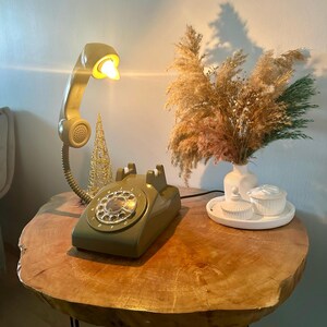 May include: A vintage green rotary phone with a white dial and a beige phone receiver lamp on a wooden table with black legs.