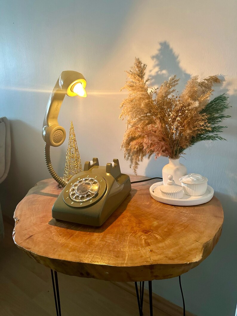 May include: A vintage green rotary phone with a white dial and a beige phone receiver lamp on a wooden table with black legs.