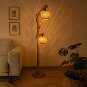 May include: A floor lamp featuring a tall, vertical wooden post base with a square bottom. Two spherical, woven rattan lampshades are attached to the post at different heights, each emitting a warm, soft glow from the internal light bulbs.