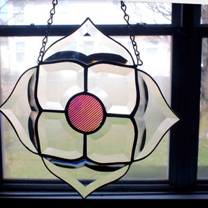 May include: A stained glass window hanging with a white background and a pink and red circle in the center.