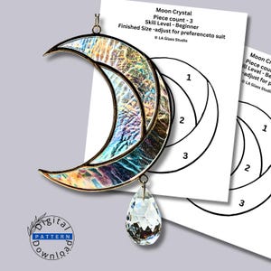 May include: A crescent moon stained glass suncatcher with iridescent, textured glass panels and a clear faceted crystal teardrop pendant. The piece includes a printed paper pattern labeled Moon Crystal, Piece count - 3, Skill Level - Beginner.