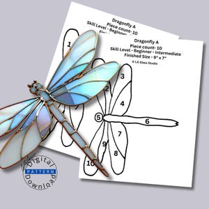 May include: A stained glass dragonfly with iridescent light blue and white wings outlined in copper foil, placed over a printed paper pattern labeled Dragonfly A, Piece count- 10, Skill Level- Beginner- Intermediate, Finished Size- 9" x 7".