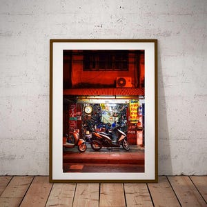 May include: A red-lit storefront in a city at night with two parked scooters in front. The storefront has a sign with Thai text and a clock on the wall.