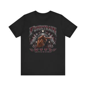 May include: Black t-shirt featuring a graphic of a train with the text "FUNKTRAIN" above a hand pointing forward. Below the hand is the text "W.T.T.D." in a stylized font. The design is in shades of red, gray, and white.