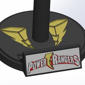 Könnte beinhalten: Ein schwarzer Sockel mit goldenen Blitzdesigns und einem schwarzen zylindrischen Stützpfeiler. Ein rechteckiges Schild mit den Worten "POWER RANGERS" in Rot und Weiß ist an der Basis befestigt.