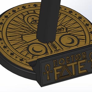 May include: A black and gold decorative stand with the words "DOCTOR FATE" and an ankh symbol. The stand has a circular top with an eye and other symbols. The base is black and the details are gold.