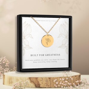 Puede incluir: Collar de oro con un colgante redondo que presenta un delicado diseño de flor. El collar viene en una caja negra con una tarjeta blanca que dice "Built for Greatness" y "With every problem you solve, you shape the future. Keep innovating, keep creating."