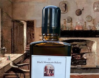 May include: A rectangular amber glass bottle with a black cap, featuring a white label with the text Black Mountain Bakery, Heavy Cream, Drip Coffee, Dark Chocolate, Perfume Oil, Mountain Lore Naturals, and 1 fl oz / 30 ml, set against a rustic room.