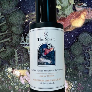May include: A perfume bottle with a black cap and a white label featuring the text "The Spirit." The label also lists ingredients: Coffee, Milk Mousse, and Lavender. The bottle is 1.7 fl oz / 50 mL. The background has a fantasy illustration.