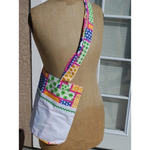 Puede incluir: Una bolsa de tela blanca con un dise&ntilde;o de patchwork en tonos de rosa, verde, azul y amarillo. La bolsa tiene una correa larga y un forro blanco.