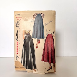 May include: A vintage sewing pattern envelope labeled 2779 with a waist size of 30 inches. The front features illustrations of three different skirt styles in blue, black, and red, along with the text Printed Pattern 25c and Simple to Make.
