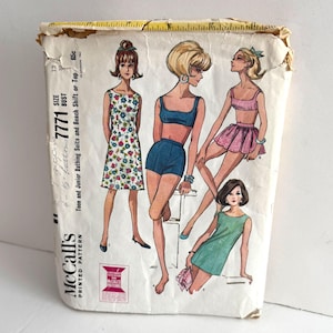 May include: Vintage McCall's printed pattern for teen and junior bathing suits and beach shifts. The illustration shows four women in various swimwear and dresses. The pattern is labeled "7771" and includes size and bust measurements.