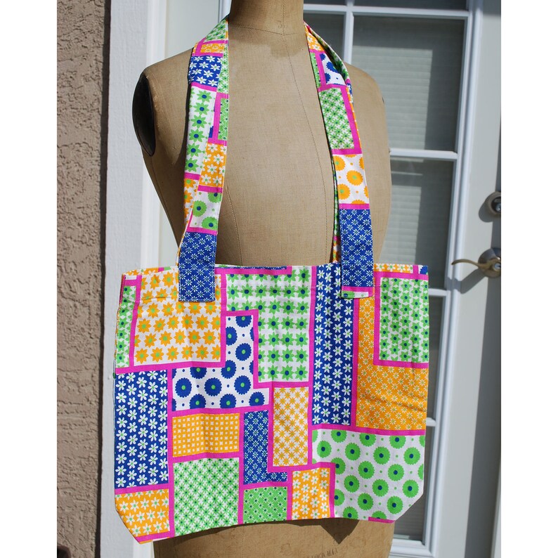 Puede incluir: Una bolsa de mano de patchwork con un patr&oacute;n geom&eacute;trico rosa, azul, verde, blanco y naranja. La bolsa tiene dos asas largas.