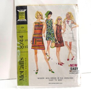 May include: Vintage McCall's sewing pattern 8744 for Misses' mini-dresses. The pattern features illustrations of four different dress styles. The package is in a plastic sleeve and has a green and white color scheme. The text on the package reads "Easy to Sew."