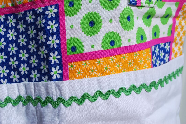 Puede incluir: Una bolsa de tela blanca con un dise&ntilde;o de patchwork que presenta varios patrones florales en tonos azules, verdes, rosas y amarillos. La bolsa tiene un ribete festoneado verde alrededor del borde superior.