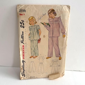May include: A vintage Simplicity sewing pattern envelope, number 2599, size 7. The front features illustrations of two pajama sets: one with a green and white striped top and pants, and another in solid light purple with ruffled collar details.