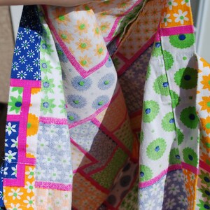 Puede incluir: Una tela de patchwork colorida con una variedad de patrones florales en tonos de rosa, azul, verde y blanco. La tela est&aacute; doblada por la mitad, revelando el reverso, que es blanco s&oacute;lido con acentos florales verdes y azules.