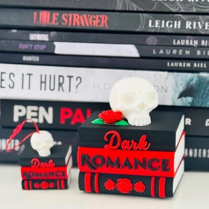 May include: Two miniature book stacks with black and red covers, each topped with a white skull and a red rose. The larger stack features the text Dark ROMANCE in red and black lettering, while the smaller stack includes a red hanging string.