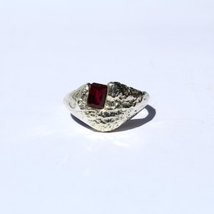 May include: A silver ring with a textured band and a red gemstone.