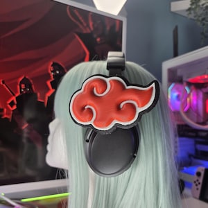May include: Black headphones with a red and white cloud emblem attached. The emblem is a stylized cloud design with a red interior and white outline. The headphones are on a mannequin head with light blue hair.