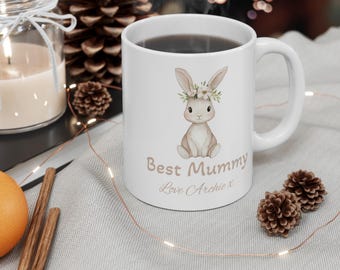 Può includere: Tazza in ceramica bianca con un coniglio marrone che indossa una corona di fiori. La tazza dice "Best Mummy" e "Love Archie x".