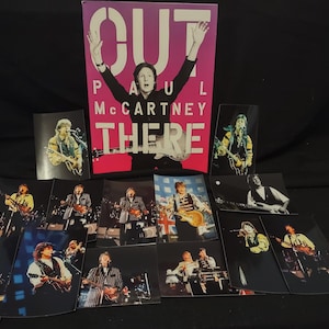 May include: A collection of concert photos and a promotional poster for Paul McCartney's "Out There" tour. The poster features McCartney with arms raised. The photos show McCartney playing guitar on stage, with various lighting and stage setups.