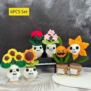 May include: A set of six crochet flower arrangements. Each flower is in a white skull-shaped pot. The flowers include sunflowers, a red rose, pink flowers, and a jack-o'-lantern. The text "6PCS Set" is in a yellow rectangle.
