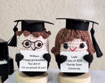 Könnte beinhalten: Zwei gehäkelte Abschlussfiguren, jede mit schwarzem Mortarboard und einem Schild. Eine Figur hat eine Brille und das Schild lautet "William Happy graduation! You did it! I'm so proud of you!". Das andere lautet "Layla Class of 2025 Florida State University."