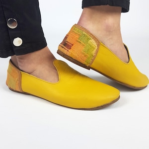 Può includere: Un paio di scarpe da uomo in pelle gialla con accenti in tessuto colorato sul retro.
