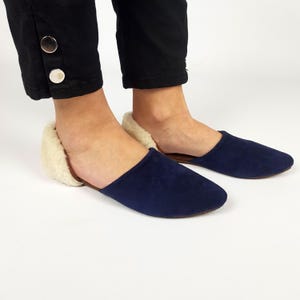 Puede incluir: Pantuflas de ante azul marino con forro de piel sintética blanca. Las pantuflas tienen una punta puntiaguda y una suela plana.