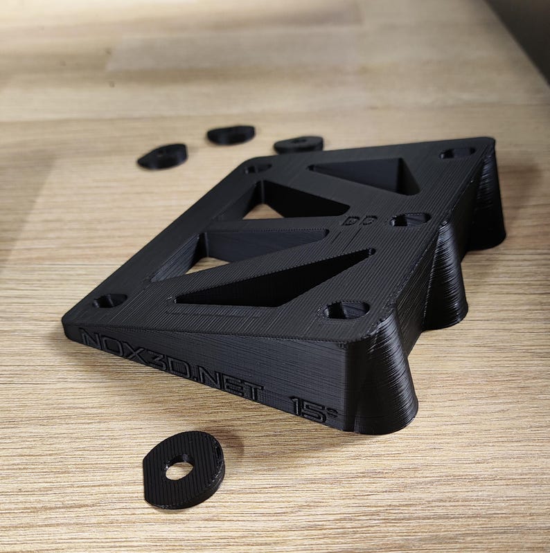 Pu&ograve; includere: Rialzo per skateboard stampato in 3D nero con il testo "NOX3D.NET 15&deg;" sul lato. Il rialzo &egrave; progettato con una forma triangolare e ha pi&ugrave; fori per il montaggio.