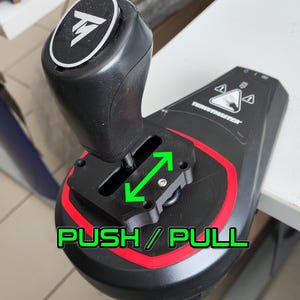 Peut inclure: Un levier de vitesses de course noir et rouge avec un logo Thrustmaster argenté. Le levier peut être poussé ou tiré, comme indiqué par les flèches vertes et le texte "PUSH / PULL".