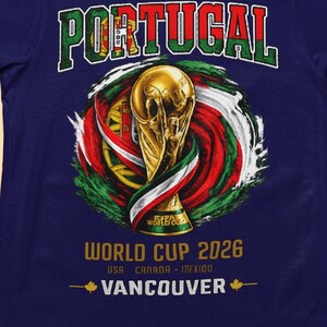 Może przedstawiać: Granatowa koszulka z napisem "PORTUGALIA" w kolorze zielono-białym, nad złotym trofeum i wirującymi czerwonymi, zielonymi i białymi akcentami. Wyświetlany jest również tekst "WORLD CUP 2026" i "VANCOUVER".