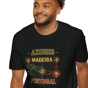Puede incluir: Camiseta negra con un diseño gráfico dorado con las palabras "AZORES", "MADEIRA" y "PORTUGAL". El diseño incluye mapas y emblemas en verde, rojo y dorado. La camiseta está hecha de un material suave.