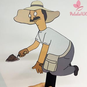 May include: A flat, cartoon-style cutout of a character wearing a wide-brimmed tan hat, a white t-shirt, and grey pants. The character has a black mustache, wears tan gloves, and holds a small trowel with a pile of brown soil. Text reads PalalaUK.