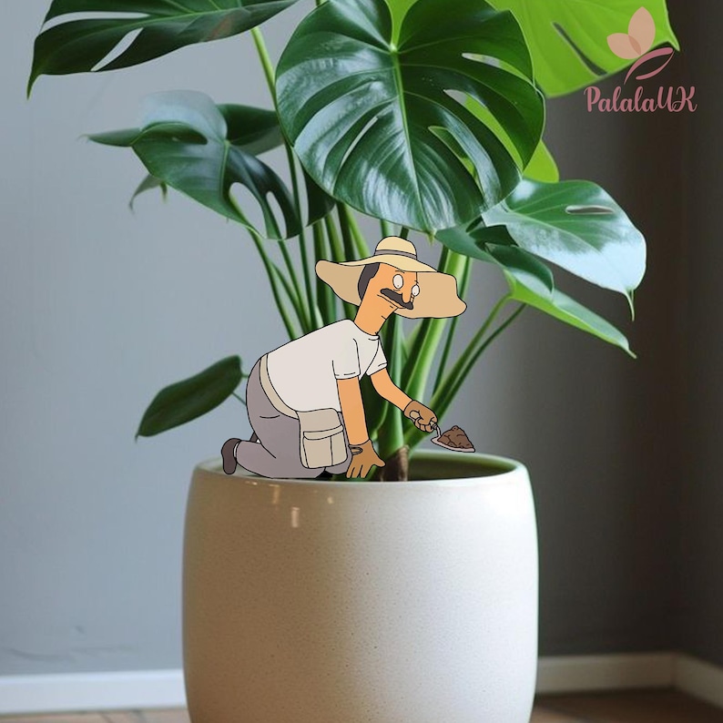 May include: A decorative plant stake featuring a cartoon character wearing a wide-brimmed tan hat, a white shirt, and gray pants, kneeling while holding a small trowel. The character is positioned in a large, smooth, light-colored ceramic planter.