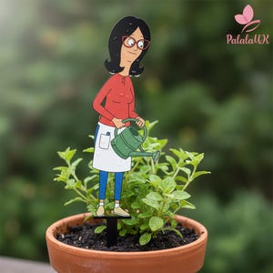 May include: A decorative plant stake featuring a cartoon character with black hair and red glasses, wearing a red long-sleeve shirt, white apron, and blue pants. The character holds a green watering can, designed to be inserted into a potted plant.