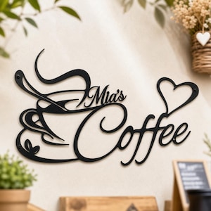 Op de afbeelding: Een zwart metalen wandbord met een gestileerde afbeelding van een koffiekop met wervelende stoom, de tekst "Mia's Coffee" in cursief schrift en een hartvorm die in het ontwerp is verwerkt. Het bord is bevestigd met zichtbare schroeven.