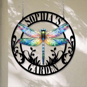 May include: A black metal circle with a cut-out design of a dragonfly and the words "Sophia's Garden".