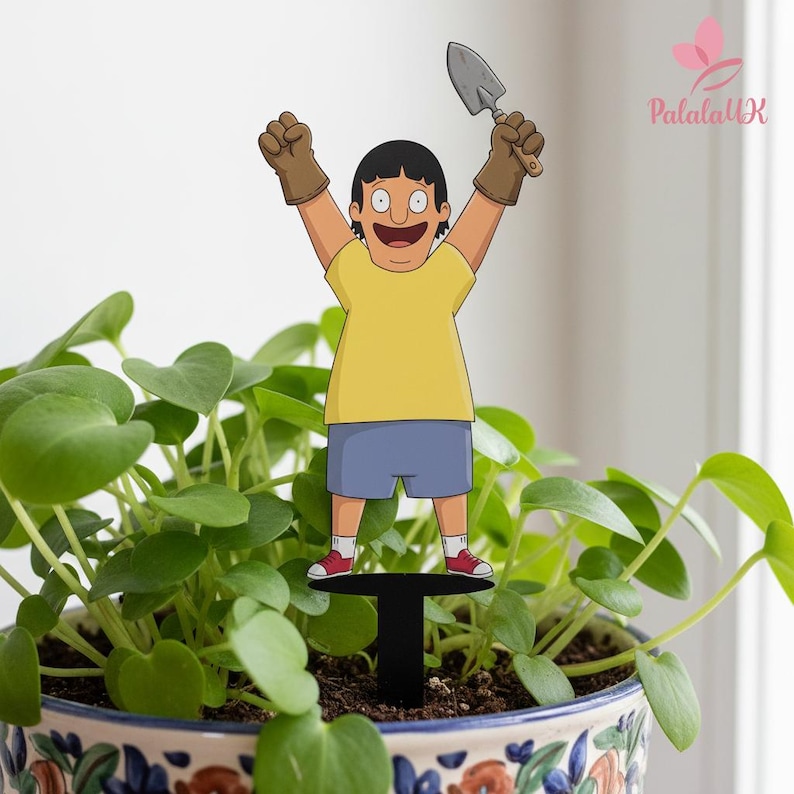 May include: A decorative plant stake featuring a cartoon character with black hair, wearing a yellow t-shirt, blue shorts, red sneakers, and brown gardening gloves. The character is holding a small grey hand trowel with both arms raised high.