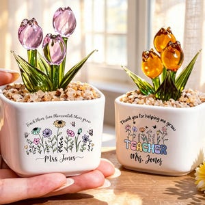 May include: Two square white ceramic planters filled with small stones and glass tulips. The left planter features purple tulips and text reading Teach them, love them watch them grow, Mrs. Jones. The right planter has orange tulips and text reading Thank you for helping me grow, TEACHER, Mrs. Jones.
