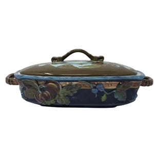 May include: An oval ceramic casserole dish with a lid, featuring a dark blue base with a raised relief pattern of fruit and leaves. The lid is brown with a central painted landscape scene and a brown handle. The dish has two side handles.